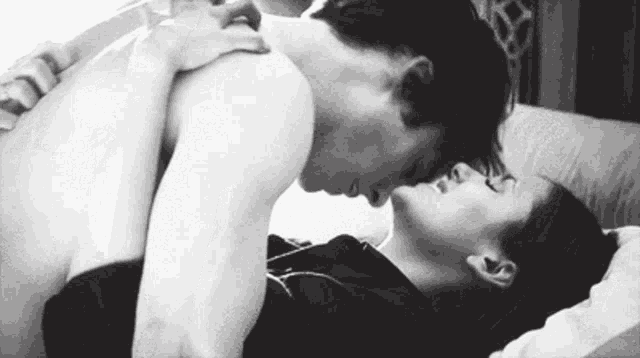 a black and white photo of a man and woman kissing in bed .
