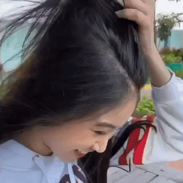 a woman with long black hair is sitting at a table with her hands on her head .