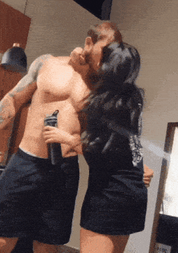 a man without a shirt is being kissed by a woman who is holding a water bottle