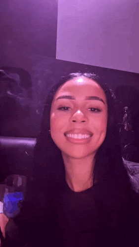 a woman with long dark hair is smiling and smoking a cigarette .
