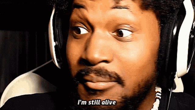 a man with a beard wearing headphones says " i 'm still alive "