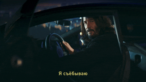 a man with long hair is driving a car with a foreign language subtitle