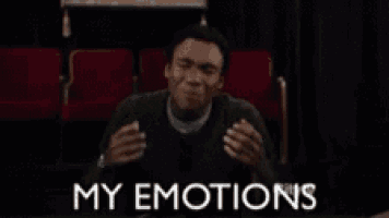 a man is sitting in a theater with his hands in the air and the words `` my emotions '' above him .