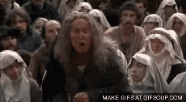 a man with long hair is standing in front of a crowd of people wearing robes .