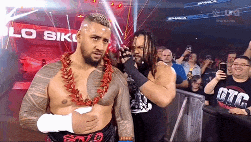 two wrestlers are standing in front of a crowd in a stadium .