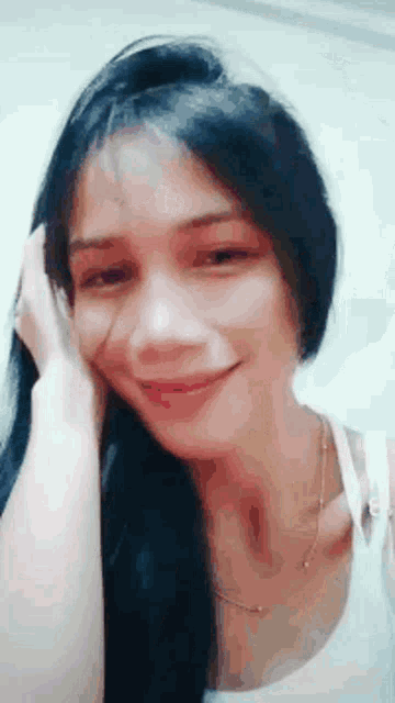 a woman with long black hair is smiling with her hand on her head .