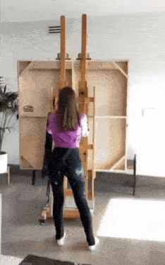 a woman in a purple shirt is standing in front of a wooden easel .