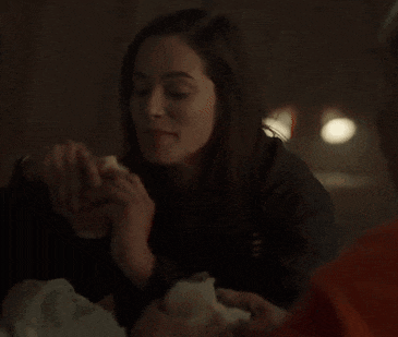 a woman is eating a sandwich in a dark room while sitting at a table .