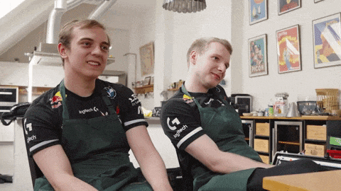 a man wearing a logitech shirt sits next to another man wearing an apron