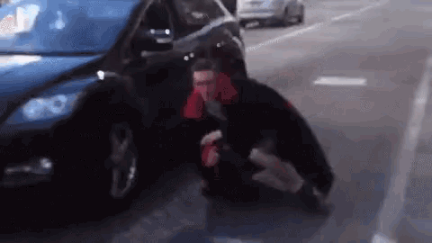 a man is kneeling down in front of a car on the side of the road .