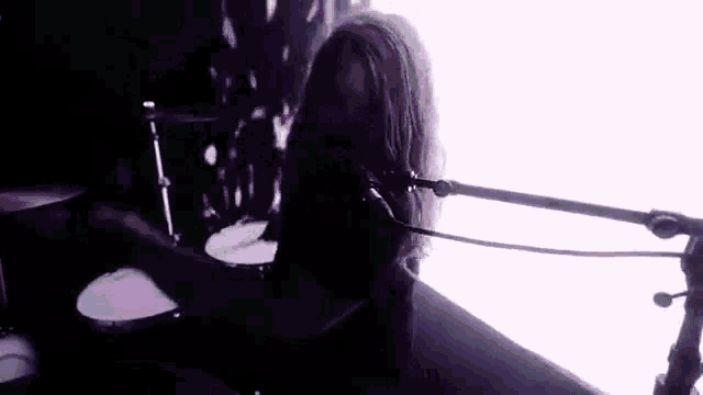 a man with long hair is playing drums in front of a microphone in a dark room .
