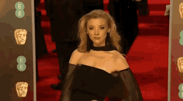a woman in a black dress is walking on a red carpet in front of a sign that says ee .