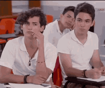 a group of young men are sitting in a classroom with their hands on their faces .