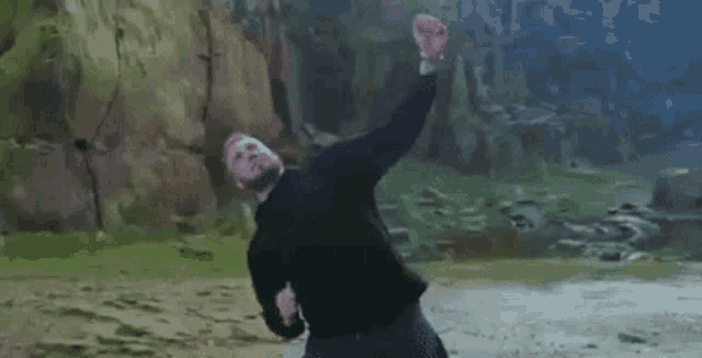 a man in a black sweater is dancing in front of a rock wall .