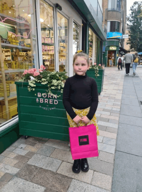 a little girl is holding a pink bag in front of a store called born bred