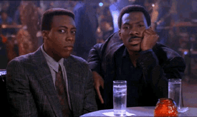 two men are sitting at a table with glasses of water in front of them