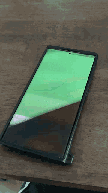 a cell phone with a green screen is laying on a wooden table