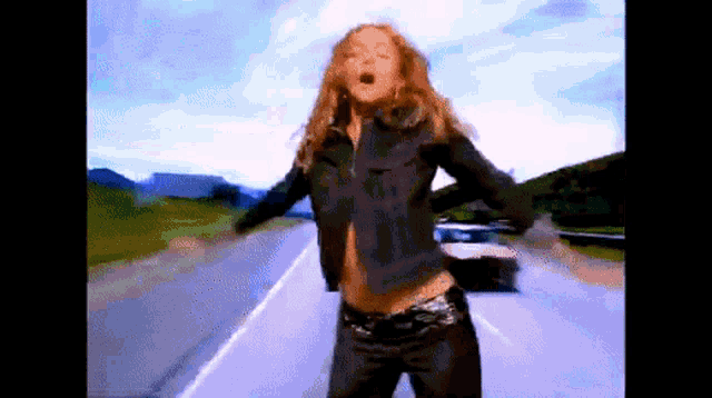 a woman in a denim jacket is standing on a road with her arms outstretched