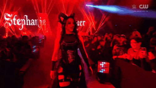 a woman in a devil costume is dancing in front of a crowd at a wrestling event .