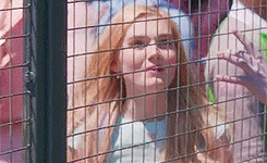 a woman with red hair is behind a fence .