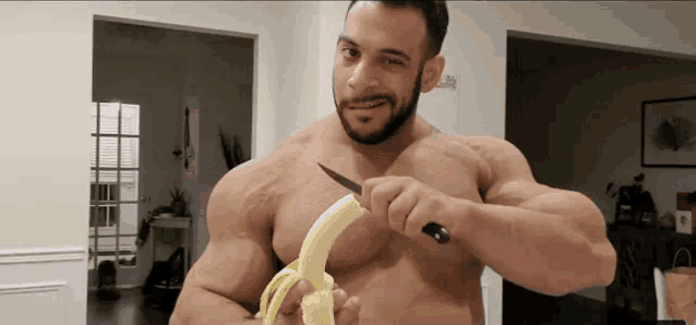 a shirtless muscular man is cutting a banana with a knife