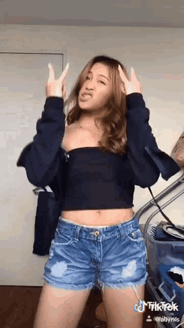 a woman in a black off the shoulder top and denim shorts is making a face