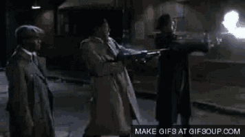a man in a trench coat is pointing a gun at another man who is holding a gun .