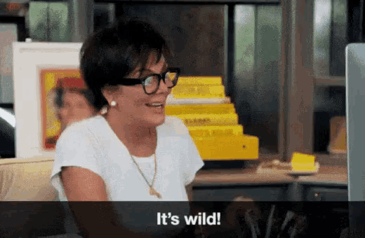 a woman wearing glasses and a white shirt is sitting in front of a computer and says it 's wild .