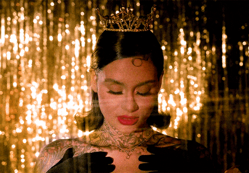 a woman wearing a crown and black gloves looks down