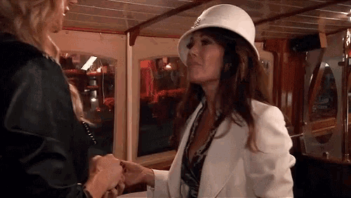 a woman in a white hat is shaking hands with another woman in a black jacket