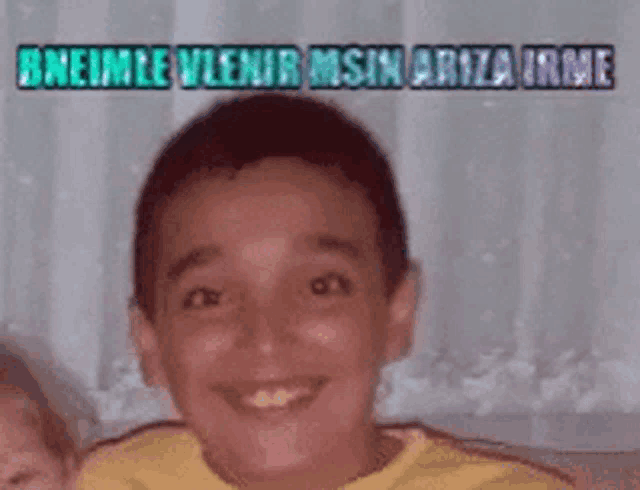 a young boy in a yellow shirt is smiling in front of a sign that says ' bnemle vlenir '