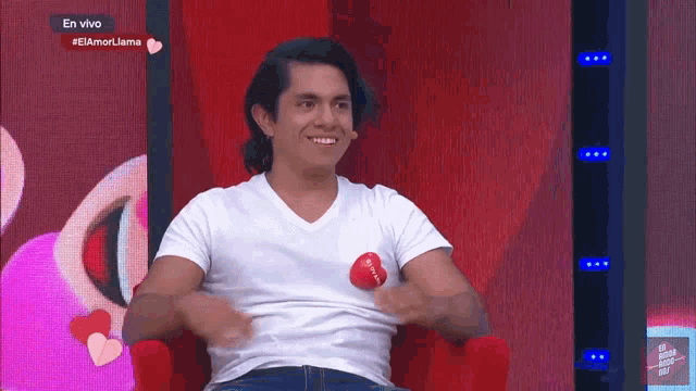 a man in a white shirt is sitting in a red chair with a red heart on his shirt that says i love you