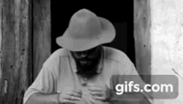 a man with a beard and a hat is sitting at a table .