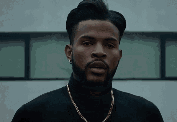 a man with a beard is wearing a black turtleneck and a gold chain