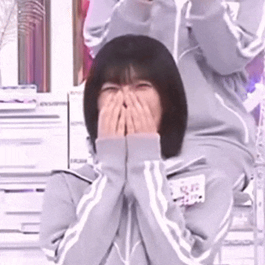 a woman is covering her face with her hands while wearing a grey jacket .