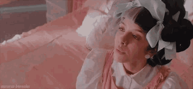 a girl with a bow in her hair is laying on a pink bed .
