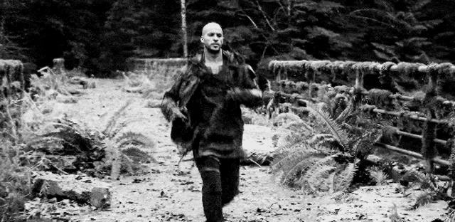 a man is walking across a bridge in the woods .