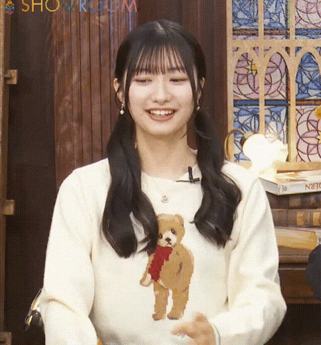 a woman wearing a white sweater with a teddy bear on it smiles