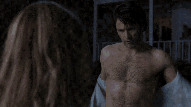 a woman in a robe stands next to a shirtless man in the dark