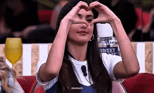 a woman is making a heart with her hands in front of a bottle of sweet water