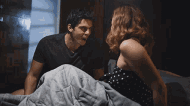 a man and a woman are sitting on a bed with the man screaming at the woman