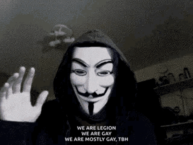 a man wearing a hooded jacket and a anonymous mask is waving his hand .