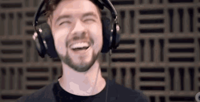 a man with a beard is wearing headphones and smiling in front of a patterned wall .