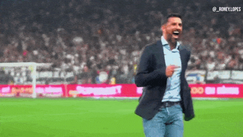 a man in a suit is standing on a soccer field with his hands in the air .