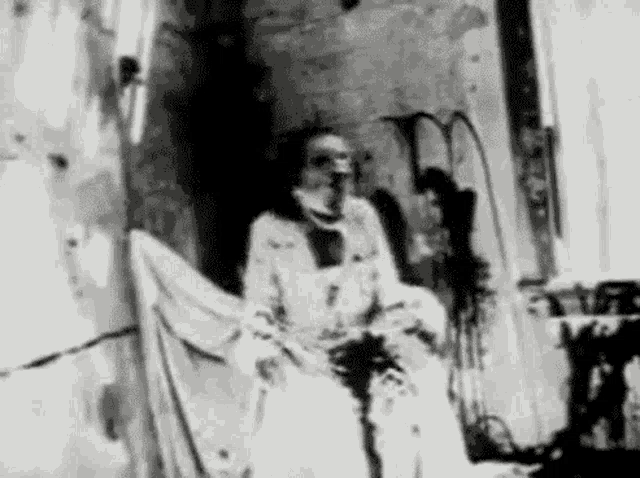 a black and white photo of a man in a white robe sitting on a chair .