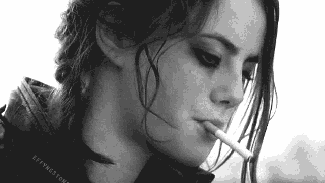a woman in a leather jacket is smoking a cigarette .