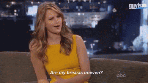 a woman in a yellow dress is sitting on a couch talking about her breasts