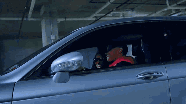 a man in a red jacket is driving a car with a woman in the back seat
