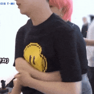 a man wearing a black t-shirt with a pixelated yellow smiley face on it is hugging another man .
