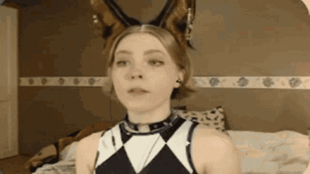 a woman wearing bunny ears and a choker is standing in front of a bed .